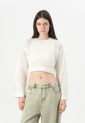 White cropped sweater with a knit pattern, featuring a round neckline and long sleeves. Worn with light green high-waisted jeans.