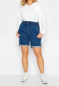 Pantalones cortos de mezclilla con cintura elástica y cordón, con puños enrollados. Combinados con una camiseta blanca y zapatillas blancas.