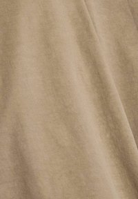 Close-up van beige stof met zichtbare zachte textuur en lichte plooien, met een fijn geweven patroon en natuurlijke vallingen.