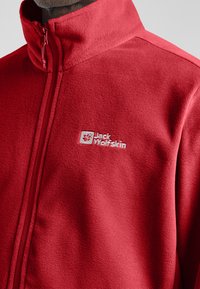 Rode fleece jas met hoge kraag en volledige rits. Voorzien van geborduurd logo op de borst. Zachte textuur, minimalistisch design en geen zichtbare patronen.