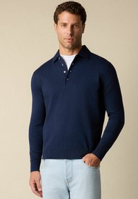 Námořnická polo košile s dlouhým rukávem, límečkem, třemi knoflíky a žebrovanými manžetami, kombinovaná se světle modrými džíny. Hladká textura.