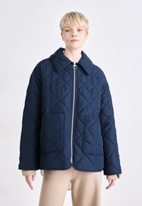 Navy quilted jacket with a large collar, front zipper, and two patch pockets. Features a diamond pattern and soft texture.