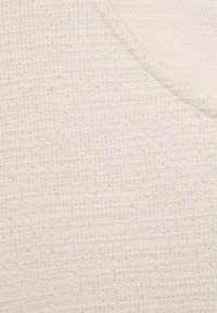 Tissu blanc texturé avec un motif tissé, présentant un léger éclat et un détail de surface variable, coupé en forme de col en V.