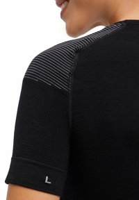 Czarny sportowy t-shirt z krótkim rękawem, wykonany z teksturowanej tkaniny, z paskami na ramionach. Wskazanie rozmiaru „L” na mankiecie rękawa.