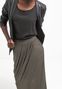 Svart satin topp kombinerad med en höggravid, draperad metallisk olivgrön kjol. Outfiten har en elegant, figurnära silhuett och mjuka texturer.