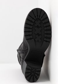 Bota negra con un exterior texturizado, suela de goma resistente con un patrón de relieve; detalle de cierre con cremallera en el lado.
