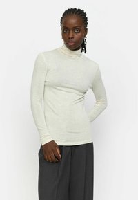 Hellcremefarbenes Langarm-Turtleneck-Top mit weicher Textur. Kombiniert mit dunkelgrauen Hosen, die eine lockere Passform und weite Beine haben.
