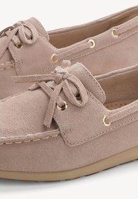 Chaussures bateau en daim beige avec lacets, couture ronde, œillets dorés et semelles en caoutchouc conçues pour un usage décontracté.
