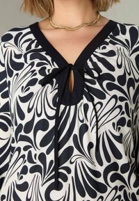 Svart- och vitblommig blus med V-ringning och knytning, samt en texturerad tyg.