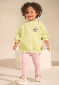 Light green sweatshirt with puffed sleeves and a playful patch, paired with pink leggings and multicolored sneakers.