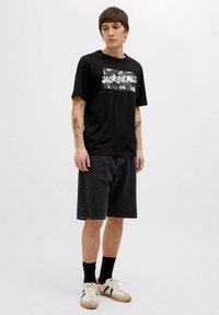 Sort t-shirt med blomster grafiktryk og logo, parret med mørke denimshorts og sneakers med accenter i grøn og rød.