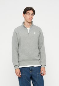 Světlě šedá mikina na zip s vysokým límcem, žebrovanými manžetami a lemem, s malým bílým logem Nike na levé hrudi.