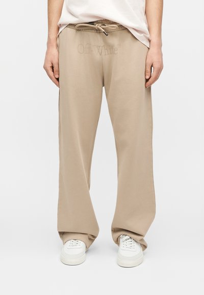 Μπεζ παντελόνι φαρδιάς γραμμής με κορδόνι στη μέση και διακριτικό λογότυπο "Off-White", συνδυασμένο με λευκά αθλητικά παπούτσια και λευκό, μέσα στη μπλούζα, πουκάμισο.