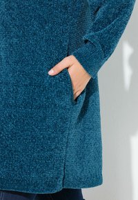 Teal texturerad tröja med lös passform, med en sidficka och ribbad ärmslut. Mjuk tyg med en mysig, varm känsla.