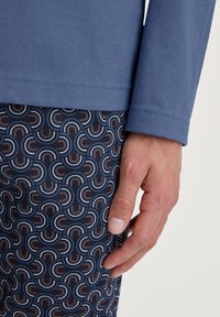 Blauwe lange mouwen shirt met ribbelstructuur, gecombineerd met gemusterde pyjamapantalons met ronde, regenboogachtige ontwerpen in rood, blauw en wit.