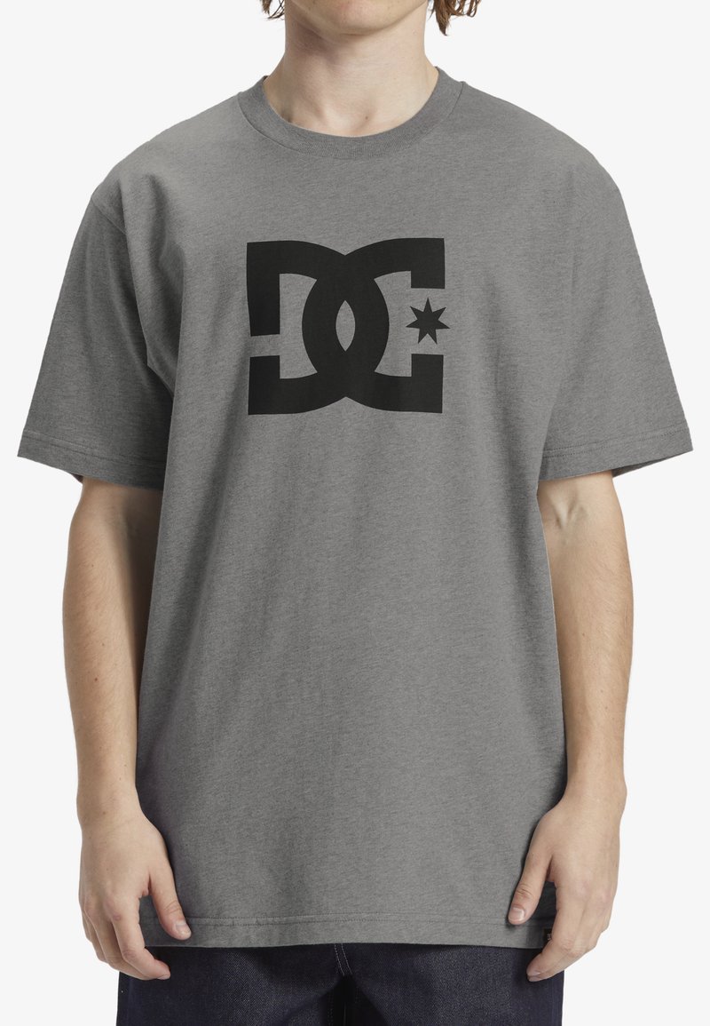 Pilkos medvilnės marškinėliai su dideliu juodu DC logotipu, dešinėje pusėje yra žvaigždės iliustracija. Trumpomis rankovėmis ir laisvumu.