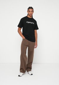 Black cotton t-shirt with "ripcurl" logo in white. Brown, wide-leg pants in soft fabric. White and black sneakers with a textured sole.