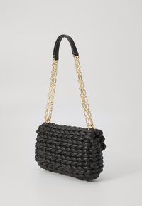 Schwarze gewebte Handtasche mit rechteckiger Form, ausgestattet mit einem massiven Kettenriemen aus goldfarbenem Metall und einer strukturierten Oberfläche.