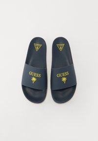 Granatowe klapki z szerokim paskiem z żółtym logo "GUESS" i wzorem palmy. Wykonane z gładkiego materiału syntetycznego.