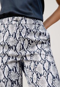 Witte en marineblauwe slangenprint broeken met een gladde textuur, voorzien van een knoopsluiting bij de taille en zijzakken.