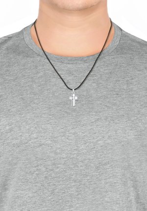 Pendentif croix en argent sur un collier en cordon noir porté sur un t-shirt gris. La croix présente une finition polie et des détails subtils.