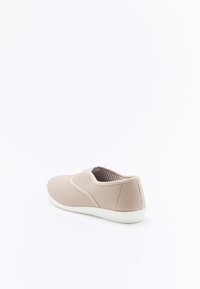 Zapato beige sin cordones con parte superior de tela texturizada, detalles laterales elásticos y suela de goma blanca. El interior presenta un patrón de rayas.