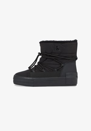 Botas de tobillo negras con suela de goma, parte superior acolchada, cordones elásticos y un borde de pelaje sintético en el cuello. Logo de Calvin Klein en relieve en el lateral.