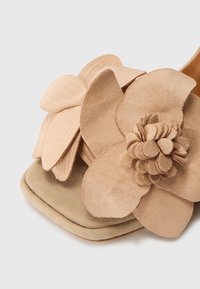 Nude suède sandaal met oversized bloemenaccenten in verschillende tinten beige, met textuur op de bloemblaadjes en een glad, rond teenontwerp.