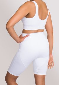 Biały prążkowany sportowy biustonosz i pasujące wysokowodne szorty, charakteryzujące się bezszwowym designem i dopasowanym krojem. Gładka tekstura z minimalną ilością detali.