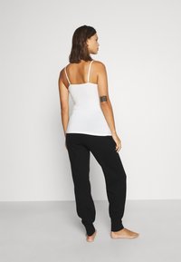 Witte tanktop met dunne bandjes en een aansluitend ontwerp, gecombineerd met zwarte trainingsbroek met een taps toelopende pijp en elastische manchetten.