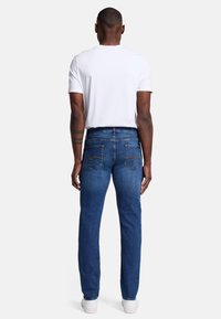 Mörkblå denimjeans med rak passform, med bakfickor med gula sömmar och en vit t-shirt.