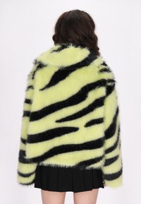 Faux fur jakke i neongul med sorte tigerstriber. Har blød tekstur og oversized pasform, med sænkede skuldre og lange ærmer.