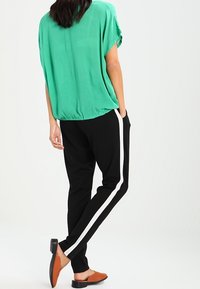 Top verde a maniche corte con vestibilità ampia, abbinato a pantaloni neri con una striscia bianca laterale. Ballerine marroni con tacco basso completano il look.