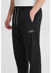 Pantalones jogger negros hechos de tejido ligero, con una cinturilla elástica y cordón, además de bolsillos laterales. Logotipo impreso en el muslo.