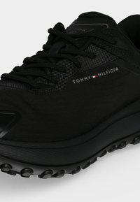 Μαύρο αθλητικό παπούτσι Tommy Hilfiger με υφή στο πλάι, σχέδιο με κορδόνια και χοντρή ελαστική σόλα με πέλματα πρόσφυσης.