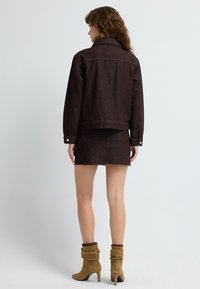 Giacca di jeans marrone abbinata a una mini gonna, con orlo sfilacciato e dettagli in bottoni dorati. Indossata con stivali marroni con tacco e dal taglio morbido.