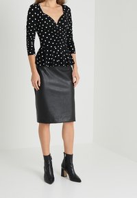 Czarna bluzka peplum w białe kropki, z długimi rękawami. Połączona z dopasowaną czarną skórzaną spódnicą. Czarne botki na kostkę z grubym obcasem.