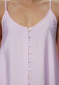 Helles lila ärmelloses Top mit V-Ausschnitt, mit einer durchgehenden Knopfleiste, die in der Mitte mit runden, schimmernden Knöpfen verziert ist.