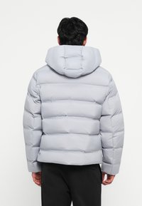 Light gray padded jacket with a hood, featuring horizontal baffles, elastic cuffs, and a smooth texture. Minimalist design and fitted shape.