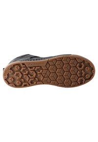 Semelle d'une botte avec une surface en caoutchouc noir texturé et un motif hexagonal marron. Affiche le nom de la marque "Vaude" et des détails de grip structuré.