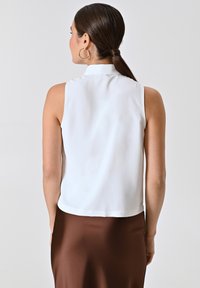 Weißes ärmelloses Oberteil mit kragen, glatter Textur und kurzem Design, kombiniert mit einem braunen Satinenrock.
