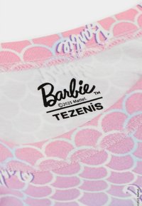 Štítek na tričko s tématem Barbie, zdobený růžovým a bílým šupinatým vzorem, s názvem značky "Barbie" a "TEZENIS" v černém písmu.