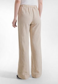 Beżowe spodnie z lnu o szerokich nogawkach z elastycznym pasem, charakteryzujące się gładką fakturą i luźnym krojem, widoczne od tyłu.