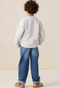Sweatshirt gris avec des poignets côtelés, associé à un jean en denim bleu large, avec des poches arrière, des poignets retroussés et des baskets multicolores.