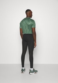 Green striped short-sleeve athletic shirt paired with black fitted leggings, featuring mesh panels and green athletic shoes with white soles.