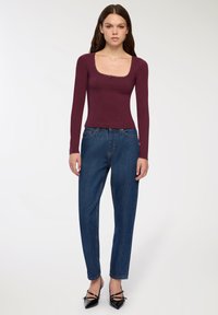 Bordowy longsleeve z dekoltem w kształcie falbany, zestawiony z luźnymi niebieskimi dżinsami i czarnymi szpilkami z długim noskiem.