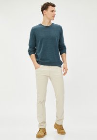 Dunkelblauem Strickpullover mit gerippten Bündchen, hellbeigen Hosen und braunen Stiefeln. Das Outfit hat einen lässigen Schnitt und ein schlichtes Design.
