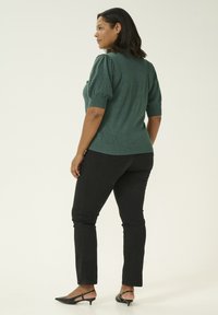 Maglione verde tessuto con maniche a sbuffo, abbinato a pantaloni skinny neri e scarpe a punta nere, visto da dietro.