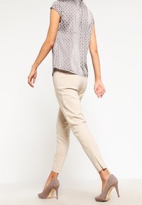 Camicia grigia con motivo e maniche corte, pantaloni beige aderenti e tacchi alti color taupe. Presenta una leggera apertura alla caviglia.