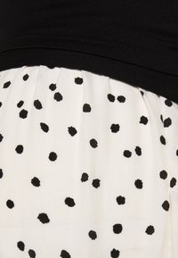 Top nero con un bodice aderente, abbinato a una gonna bianca con pois neri sparsi, realizzata in un tessuto leggero e testurizzato.